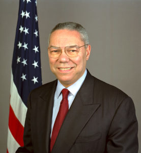 A formal picture of Gen. Colin Powell sitting in front of a flag. 